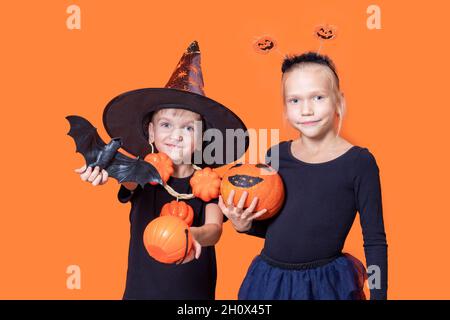 Un trucco per bambini o una delizia in un costume di Halloween. Ragazzino in un cappello del mago che tiene un cestino arancione a forma di zucca, un pipistrello nero e una presa ragazza Foto Stock