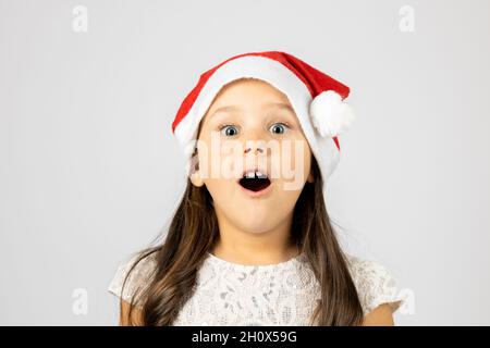 Primo piano ritratto di sorpresa, scioccato, open-mouthed ragazza in rosso Babbo Natale cappello, isolato su sfondo bianco con spazio copia Foto Stock