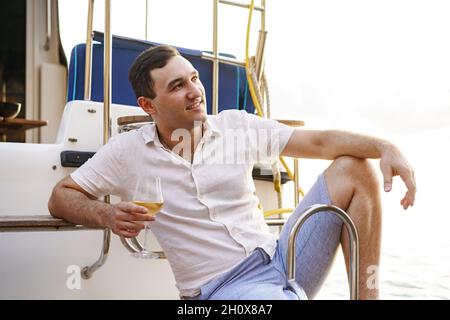 Giovane uomo che tiene un bicchiere di vino su un ponte aperto di una nave da crociera Foto Stock