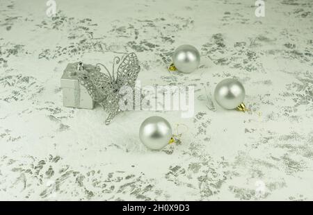 Composizione di Natale sullo sfondo bianco originale di Capodanno. Scatola regalo in argento - giocattolo, farfalla lucente openwork e palline in argento Foto Stock