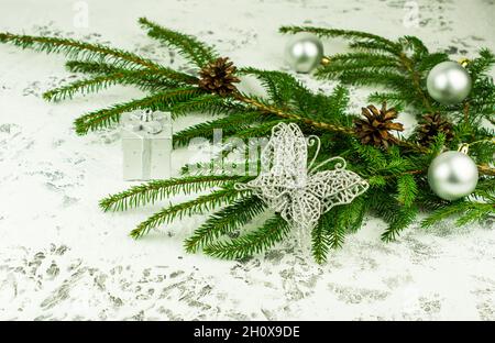 Decorazione di Capodanno della casa con un ramo verde di abete rosso con coni con palle lucide e farfalla d'argento openwork. Sfondo bianco neve Foto Stock