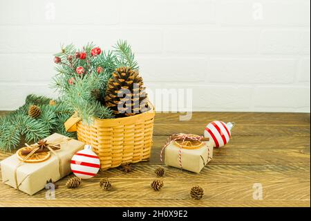 Decorazione festosa per la casa a Natale. Cestino di vimini con rami di abete rosso e bacche, cono di cedro e scatole regalo su un tavolo di legno Foto Stock