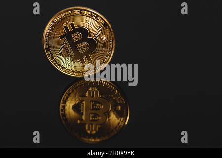 Primo piano bitcoin dorato con riflesso isolato su sfondo nero. Bitcoin si riflette nello specchio. Foto Stock