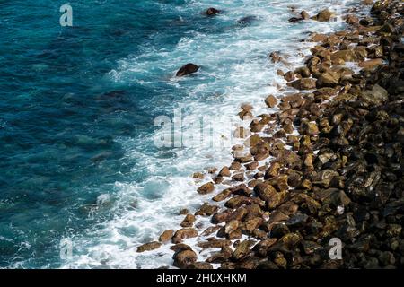 le onde dell'oceano colpiscono la spiaggia di pietra nera, il paesaggio roccioso della costa Foto Stock