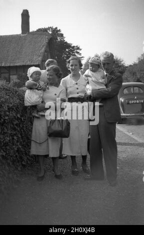 Alla fine degli anni '1940, una famiglia con bambini in piedi per una foto fuori da una casa di paglia, Anne Hathaway's Cottage, la casa d'infanzia della moglie del famoso scrittore inglese William Shakespeare, a Shottery appena fuori Stratford-upon-Avon, Inghilterra, Regno Unito. Auto dell'epoca parcheggiata sulla corsia. Foto Stock