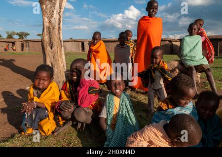 Un gruppo di ragazzi Masai si radunarono vicino ad un albero fuori dal loro villaggio. Masai Mara National Reserve, Kenya. Foto Stock