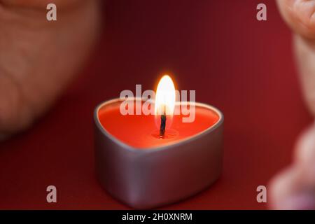Le mani femminili che tengono una candela a forma di cuore in primo piano scuro Foto Stock