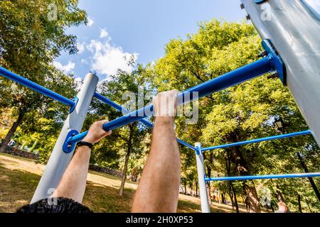 Un uomo si tirerà su sbarre orizzontali su un terreno sportivo. Foto Stock
