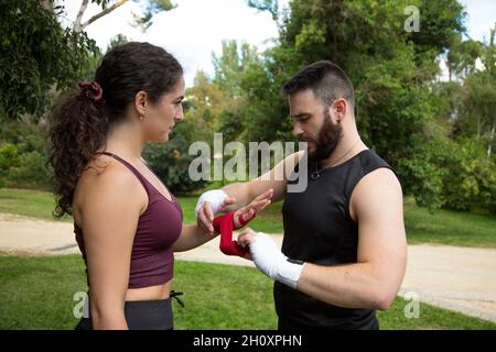 Giovane allenatore di boxe caucasico bearded che mette i guanti di boxe sulla giovane donna Foto Stock