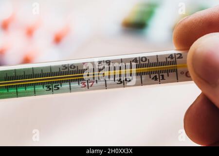 termometro a mercurio isolato sulla mano dell'uomo su sfondo blu.  Misurazione della temperatura mediante un termometro. Febbre alta e  malattia. Primo piano Foto stock - Alamy