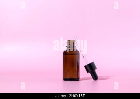 Bottiglia di vetro marrone con contagocce su sfondo rosa. Imballaggio di siero o olio essenziale. Mockup di un prodotto cosmetico. Vista frontale con spazio di copia. Foto Stock