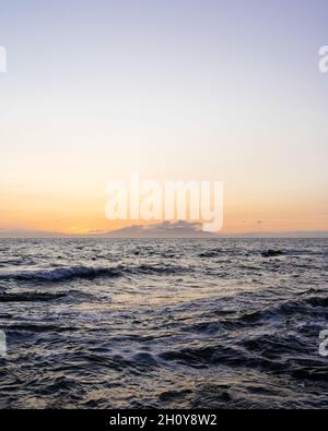 Vista al tramonto dell'isola scozzese di Arran attraverso il mare da Troon AT con la catena montuosa Goatfell all'orizzonte illuminata dal sole del tramonto. Foto Stock