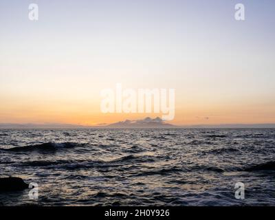 Vista al tramonto dell'isola scozzese di Arran attraverso il mare da Troon AT con la catena montuosa Goatfell all'orizzonte illuminata dal sole del tramonto. Foto Stock