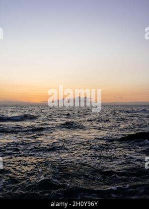 Vista al tramonto dell'isola scozzese di Arran attraverso il mare da Troon AT con la catena montuosa Goatfell all'orizzonte illuminata dal sole del tramonto. Foto Stock