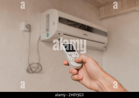 La mano del ragazzo tiene il telecomando del condizionatore d'aria. Raffreddamento e controllo della temperatura nella stanza della casa. Foto Stock