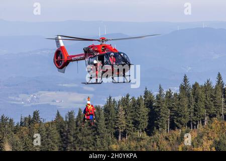 Waldkirch, Germania. 15 ottobre 2021. Un membro ciascuno del Bergwacht e del DRF Luftrettung appende su una corda sotto un elicottero di salvataggio, mentre la Foresta Nera può essere visto sullo sfondo. Durante l'addestramento del verricello, l'equipaggio della stazione di Friburgo della DRF Luftrettung (cartello di chiamata Christoph 54) pratica le operazioni con il verricello sotto un elicottero insieme al Black Forest Mountain Rescue Service. Credit: dpa/Alamy Live News Foto Stock