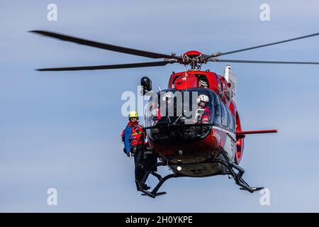Waldkirch, Germania. 15 ottobre 2021. Un membro della squadra di soccorso in montagna si erge sulle piste di un elicottero di soccorso. Durante l'addestramento del verricello, l'equipaggio della stazione di Friburgo della DRF Luftrettung (cartello di chiamata Christoph 54) pratica le operazioni con il verricello sotto un elicottero insieme al Black Forest Mountain Rescue Service. Questo verricello può essere utilizzato per salvare i pazienti da terreni impraticabili, nonché per trasportare medici e paramedici in regioni difficili da raggiungere. Credit: Rin/dpa/Alamy Live News Foto Stock