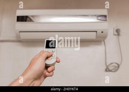 La mano del ragazzo tiene il telecomando del condizionatore d'aria. Raffreddamento e controllo della temperatura nella stanza della casa. Foto Stock