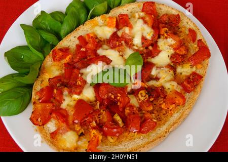 Deliziosa bruschetta italiana con succosi pomodori rossi, mozzarella, aglio, olio d'oliva e foglie di basilico fresco su un piatto Foto Stock