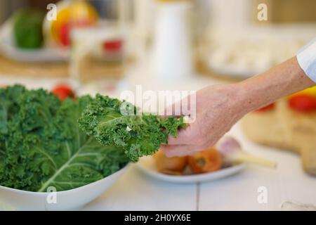 Vecchia donna irriconoscibile che prepara l'insalata di verdure mentre cucinano il cibo in cucina a casa Foto Stock