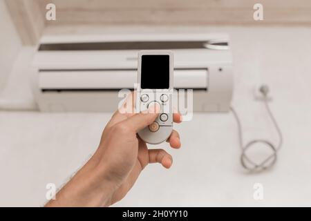 La mano del ragazzo tiene il telecomando del condizionatore d'aria. Raffreddamento e controllo della temperatura nella stanza della casa. Foto Stock