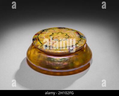 Scatola coperta, c. 1898–1902. Tiffany Glass & Decorating Company (American, New York, 1892–1902). Vetro Favrile, smalto su rame; 14 cm (1/2 poll.). Nel 1900 Tiffany aveva ampliato il suo impero aumentando la produzione della società di “beni di fantasia”, compresi pensiline, candelieri, orologi, scatole piccole, set da tavolo, schermi per tè e altri oggetti funzionali. Insieme con la serie di disegni artistici di vetro dalla sua fabbrica a Corona, Queens, lavori in ceramica, bronzo, altri metalli, e persino i monili abbondavano. Questi oggetti di lusso più piccoli e più accessibili sono stati progettati con tanto pensiero per l'arte come il Foto Stock