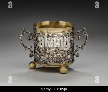 Tazza a due maneggiate, 1677. Inghilterra, Londra, XVII secolo (Carlo II). Argento e argento dorato; totale: 17.2 x 11.5 cm (6 3/4 x 4 1/2 pollici). A causa delle sue dimensioni e ornamento, questo vaso può aver funzionato come una tazza di caudle, contenente una miscela di birra o vino e pane, farinata d'avena, uova, zucchero e spezie che è stato dato alle donne dopo il parto per aiutarli a riguadagnare la loro forza. Il fogliame a scorrimento e gli uccelli esotici lungo l'esterno di questa tazza erano probabilmente basati su stampe circolanti nel 1600. Le figure femminili reclinabili che tappano le maniglie e l'acantus gemma finiale sul coperchio di accompagnamento re Foto Stock