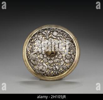 Coperchio per una tazza a due maneggiate, 1677. Inghilterra, Londra, XVII secolo (Carlo II). Argento e argento dorato; totale: 17.2 x 11.5 cm (6 3/4 x 4 1/2 pollici). A causa delle sue dimensioni e ornamento, il recipiente che accompagna questo coperchio può aver funzionato come una tazza caudle, contenente una miscela di birra o vino e pane, farinata d'avena, uova, zucchero e spezie che è stato dato alle donne dopo il parto per aiutarli a riguadagnare la loro forza. Il fogliame a scorrimento e gli uccelli esotici lungo l'esterno della tazza erano probabilmente basati su stampe circolanti nel 1600. Le figure femminili reclinabili che tappano le maniglie e il germoglio di acanto f Foto Stock