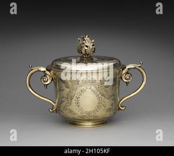 Tazza a due manine e coperchio, 1686. Inghilterra, Londra, XVII secolo (Giacomo II). Dorato argento; totale: 23.9 x 32.4 cm (9 7/16 x 12 3/4 pollici). Prodotto un anno dopo l'incoronazione di Giacomo II (1633-1701), questa coppa d'argento celebra la monarchia e riflette le alleanze politiche e sociali che hanno sostenuto l'aristocrazia durante il 1600. Durante la loro incoronazione, Giacomo II e la sua seconda moglie Maria di Modena (1658-1718) furono trasportati attraverso la città di Londra sotto un baldacchino di seta adornato da motivi ispirati alle percezioni europee dell'arte cinese, nota come chinoiserie. Dopo la processione, la t Foto Stock