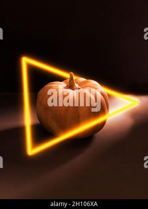 Zucca arancione con luce al neon su sfondo nero. Atmosfera mistica. Orientamento verticale. Foto Stock