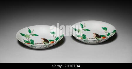 Piatto con uccello su Peach Branch, 1662-1722. Cina, provincia di Jiangxi, forni Jingdezhen, dinastia Qing (1644-1911), marchio e regno di Kangxi (1662-1722). Porcellana con decorazione a smalto vetrificato a base di famille-verte; diametro: 20.7 cm (8 1/8 in.); recipiente: 2.5 cm (1 in.). Tra i più grandi successi delle prime porcellane Qing ci sono i prodotti da tavola e oggetti espositivi decorati con pittura policroma come questo paio di piatti. Caratterizzato da uccelli arroccati in peschi, i piatti sono legati al famoso compleanno stabilito per il sessantesimo compleanno dell'imperatore Kangxi nel 1713. Questi pezzi sono più inventivi Foto Stock