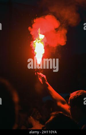 Torcia rossa nelle mani di un uomo che si trova di fronte al palco di un festival di musica rock. Una folla di tifosi in un concerto Foto Stock