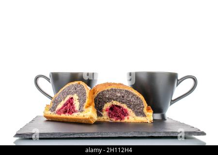 Due pezzi di strudel di papavero di ciliegia su una pietra d'ardesia con due tazze nere, primo piano, isolato su bianco. Foto Stock