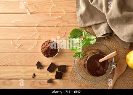 Cioccolata calda in paese crema di cioccolato in bicchiere di vetro su tavoletta di legno con pezzo e polvere di cioccolato. Vista dall'alto. Composizione orizzontale. Foto Stock