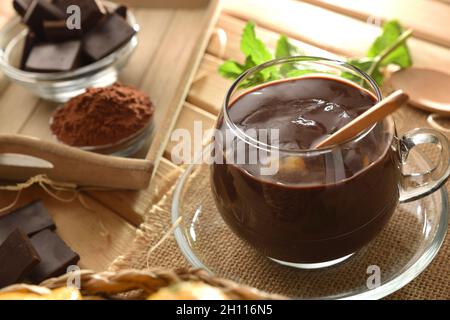 Cioccolato liquido country in una tazza di vetro su un tavolo di legno con un pezzo e polvere di cioccolato. Vista rialzata. Composizione orizzontale. Foto Stock