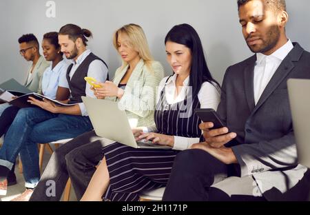 Gente multirazziale che usa i laptop e i cellulari mentre aspetta in linea per l'intervista di lavoro Foto Stock