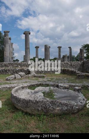 Il Macellum o mercato: In primo piano un'antica macina di un mulino e sullo sfondo le colonne della Basilica. Sepino, Molise, Italia Foto Stock