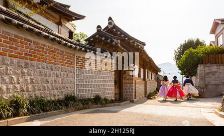 Tre giovani donne in hanboks colorati che camminano lungo la strada nel villaggio di Bukchon Hanok a Seoul. Foto Stock