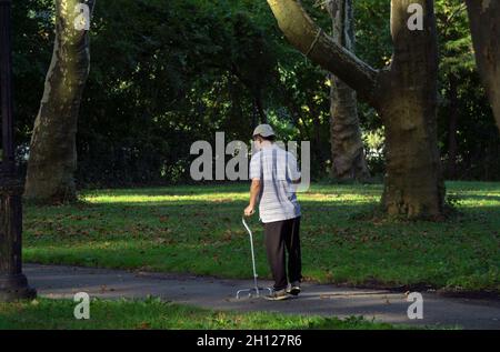 Un uomo più anziano che cammina con una canna a quattro zampe su un sentiero panoramico. In un parco nel Queens New York in una soleggiata giornata autunnale. Foto Stock