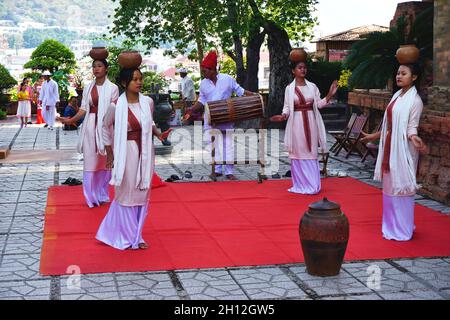 Le giovani donne vietnamite in bei costumi eseguono una danza etnica tradizionale su un tappeto rosso accanto all'antico tempio Cham, Nha Trang, Vietnam Foto Stock