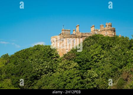 Il castello di Culzean sbircia tra gli alberi, visto dalla spiaggia del South Ayrshire, sulla costa occidentale della Scozia. Foto Stock