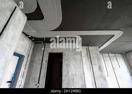 Cavi e tubi elettrici su soffitti e pareti in cemento. Tubi flessibili e condotti in plastica moderni con fili in camera. Linee dei tubi di cablaggio in pvc dopo Foto Stock