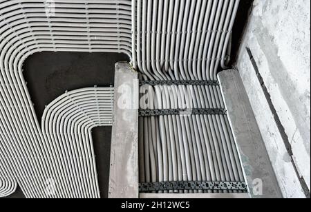 Cavi e tubi elettrici su pareti e soffitti in calcestruzzo. Tubi flessibili e condotti in plastica moderni con fili in camera. Linee dei tubi di cablaggio in pvc dopo Foto Stock