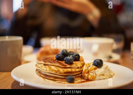 Pancake dolci con sciroppo al caramello, mirtilli e gelato sul piatto del caffè Foto Stock