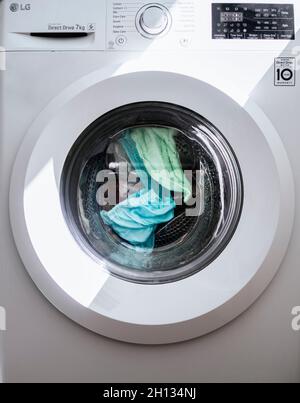 Vestiti blu e verde che girano in lavatrice a carico laterale Foto Stock
