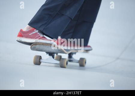 Ragazza pattinatore che rotola su una rampa di cemento nel parco skate all'aperto. Atleta di skateboarder femminile con scarpe rosse Foto Stock