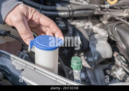 sistema lavacristallo di manutenzione all'interno della vettura. La mano maschio del meccanico dell'automobile apre il tappo del serbatoio del lavacristallo sotto il cofano Foto Stock