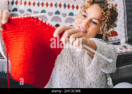 Donna adulta attraente a casa in attività di lavoro a maglia utilizzando lana colorata. Le donne sono felici e rilassate e godono di un po' di tempo al coperto sul divano. Maglia j Foto Stock