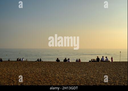 Un sacco di persone che siedono sulla spiaggia in silhouette contro il mare in incandescente sole di ottobre pomeriggio, Hove, East Sussex, Inghilterra. Foto Stock