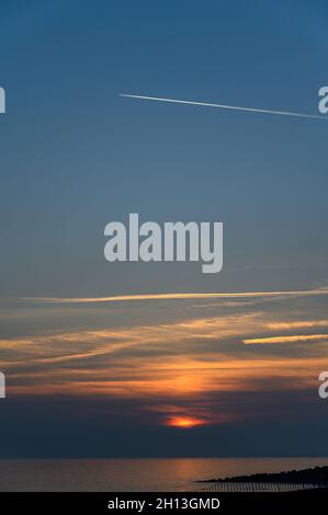 Tramonta sulla costa del Sussex con il controtail di un aeroplano che attraversa un grande cielo blu. Hove. Sussex orientale, Inghilterra. Foto Stock